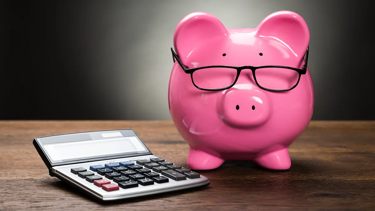 A pink piggy bank with glasses next to a calculator